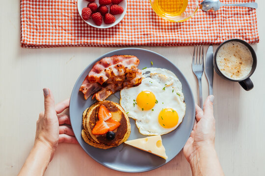 Anonymous crop hands putting plates with delicious fried eggs with bacon and cheese on table for breakfast