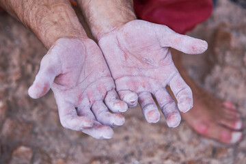 From above view of crop hands covered with white chalk powder of unrecognizable barefoot male alpinist after hard ascending on rocky cliff