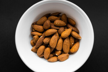Almonds in a small plate on a black table. Almond is a healthy vegetarian protein nutritious food....