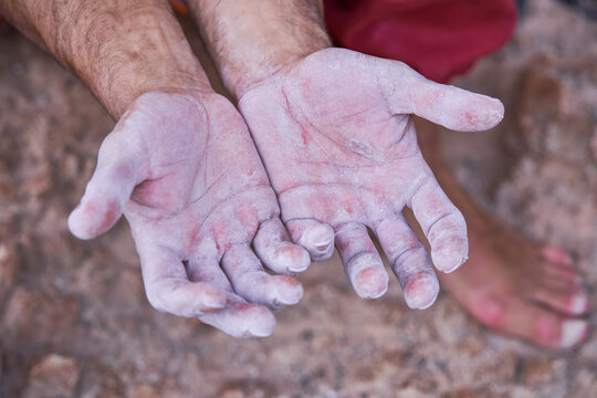 From above view of crop hands covered with white chalk powder of unrecognizable barefoot male alpinist after hard ascending on rocky cliff