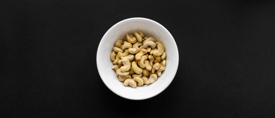 Obraz na płótnie Canvas Cashew nuts in a small plate on a black table as a background. Cashew nut is a healthy vegetarian protein nutritious food.