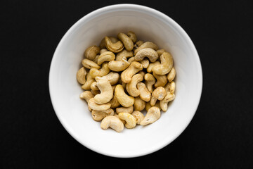 Cashew nuts in a small plate on a black table as a background. Cashew nut is a healthy vegetarian protein nutritious food.