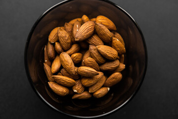 Almonds in a small plate on a black table. Almond is a healthy vegetarian protein nutritious food. Natural nuts snacks.