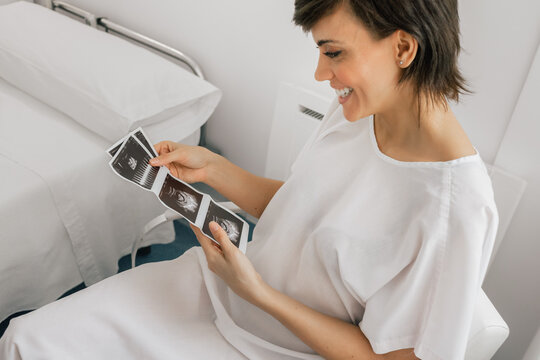 From above pregnant female inspecting sonogram picture while sitting in a chair in ward of modern fertility clinic