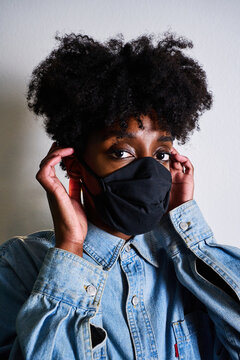 Young African American female in casual denim shirt and black protective mask looking at camera while staying at home during coronavirus outbreak