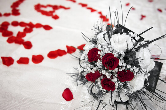 Classic bridal bouquet with dark red and white roses, heart of rose petals in the background and initial letters AA. Wedding concept and partial desaturation.