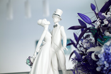 Figurines in love with the bride and groom, ceramic sculpture, with wedding rings for the wedding day, purple fantasy flower arrangement in the foreground.