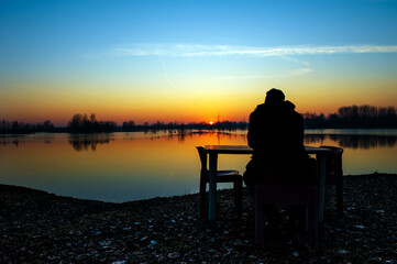 Obraz premium View of a person sitting and admiring the beautiful colors at sunset on the lake on a winter day.