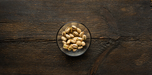 Obraz na płótnie Canvas Pistachios in a small plate on a vintage wooden table. Pistachio is a healthy vegetarian protein nutritious food. Natural nuts snacks.