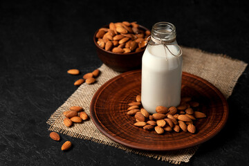 one bottle of almond milk on a dark black background with nuts, vegetarian milk without sugar and lactose