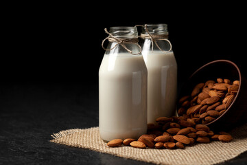 almond milk in bottles with nuts on a dark black table, a variety of dairy products without sugar and lactose