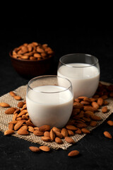 almond milk with glasses on sprinkled nuts, vegetarian milk drink without lactose against a dark background, close-up