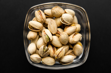 Pistachios in a small plate on a black table. Pistachio is a healthy vegetarian protein nutritious...