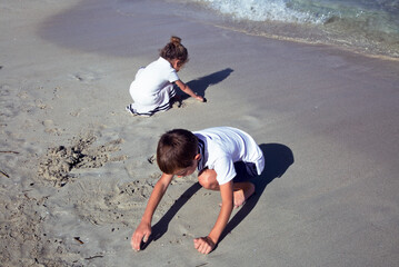 Two kids are drawing on the sand by the sea