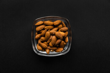 Almonds in a small plate on a black table. Almond is a healthy vegetarian protein nutritious food. Natural nuts snacks.