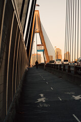 Person walking lonely along a cable suspended bridge with cityscape in the background