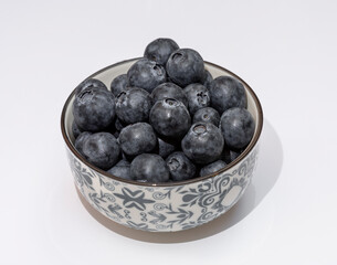 Fresh aromatic blueberries in a porcelain cup on a white background