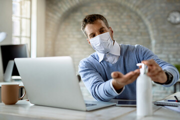 Male entrepreneur with protective face mask using hand sanitizer in the office.