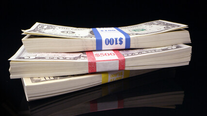 Stacks of money on black surface with 1, 5, and 10 dollar bills.