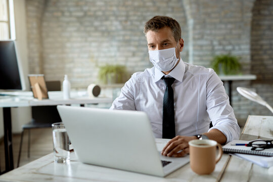 Businessman working on laptop while wearing protective face mask in the office.