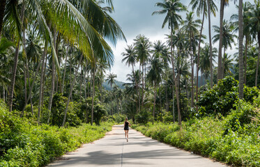 Happy young woman run on the jungle's empty road with a coconut palm trees. Vacation and travel concept.
