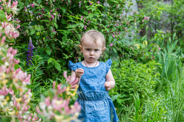 Beautiful little cute blond girl sniffing flowers in the garden.