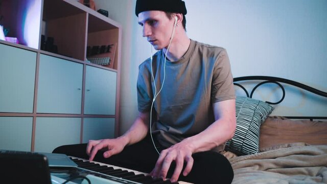 Young caucasian guy sitting in his bedroom and playing on MIDI keyboard or synthesiser and making electronic music.Dj slow motion footage