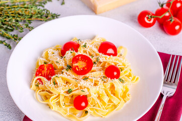 Homemade fettuccine pasta with tomatoes, thyme, parmesan cheese in a white plate on a light background.