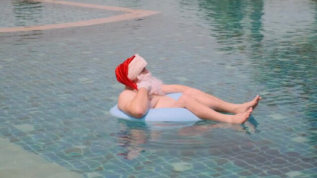 Santa Claus floating on inflatable ring in swimming pool on sunny day enjoying tropical New Year.