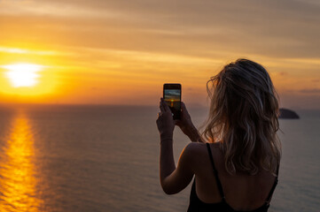 Woman hands holding mobile phone at sunset. Young curly hair woman taking photos with her cell...