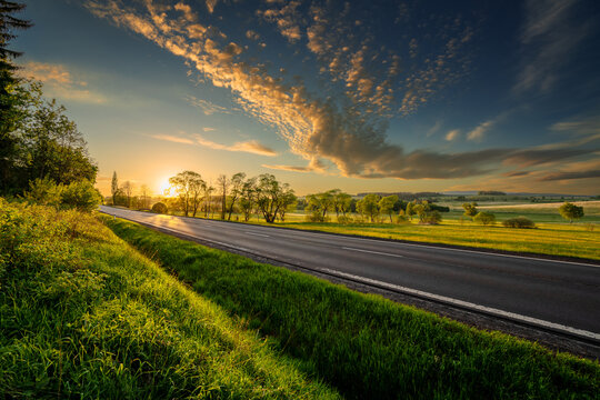 Empty asphalt road in rural landscape at sunset