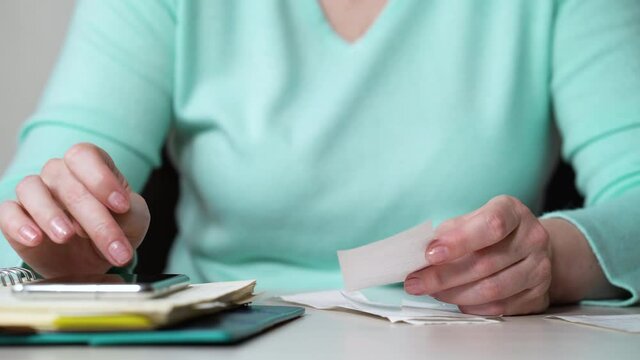 Female hands calculating sums of supermarket bills and writing in notebook