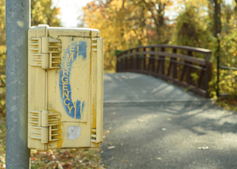 A yellow emergency call box station on a walking and biking trail.