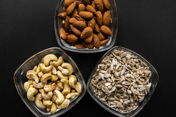 Almond, cashew and sunflower seeds in a small plates which standing on a black table. Nuts is a healthy vegetarian protein and nutritious food.