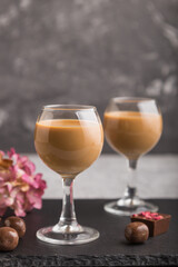 Sweet chocolate liqueur in glass on a gray concrete background and black stone slate board. Side view, selective focus.