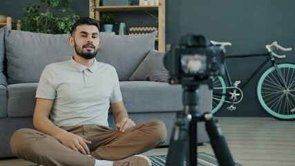 Slow motion of cheerful Arab man vlogger recording video with camera for vlog in social media speaking and gesturing waving hand sitting on floor alone.