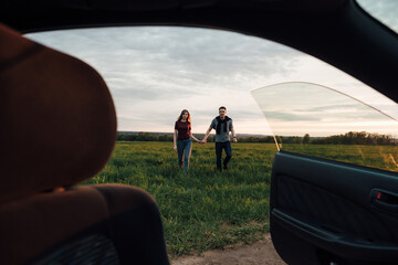 young fashionable loving couple are walking and having fun in a forest field at sunset dawn near the car