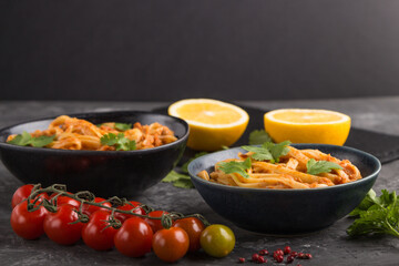 Semolina pasta with tomato pesto sauce, orange and herbs on a black concrete background. Side view, selective focus, copy space.