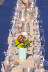 Long table with blue table cloth and burlap center runner, wine glasses set out and flowers and candles