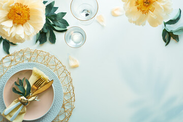 Contemporary table setting with peony flowers and golden utensils on white table. Modern trendy...