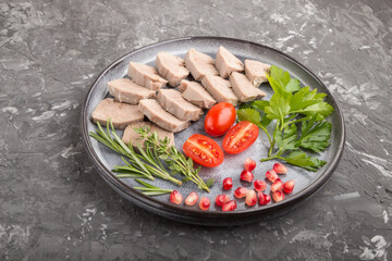 Boiled pork tongue with tomatoes and herbs on a black concrete background. Side view, close up.