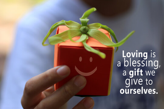 Inspirational motivational quote - Loving is a blessing, a gift we give to ourselves. With hand holding an orange gift box with happy smiling face emoticon and a green cananga odorata flower on it. - Powered by Adobe