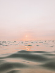 Low angle shot in ocean waves with pink and orange sunset in the background