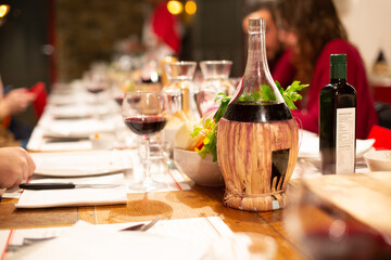 Table with red wine bottle, glasses with snacks and people eating