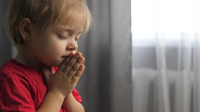 little daughter girl makes a wish prayers bedtime religion lifestyle concept . prayer child indoors praying by bed in front of window