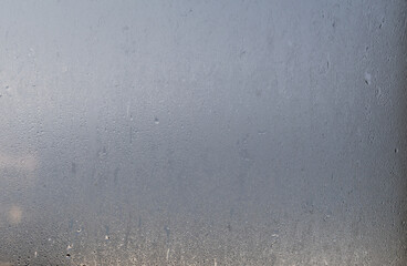 Morning rain drops on a glass window with blurred blue sky background, view through a wet and sweaty window with a cope and text space
