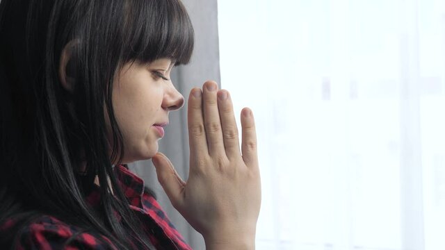 brunette girl makes a wish prayers bedtime religion concept. prayer woman lifestyle mom indoors praying by bed front of window