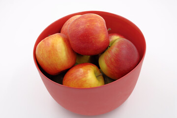 Red apples in red glass fruit bowl, isolated.