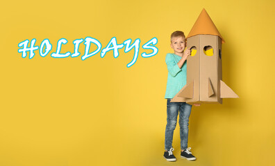 School holidays. Cute little child playing with cardboard rocket near yellow wall. Banner design