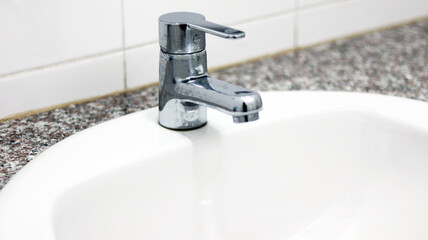 The Silver Faucet with white ceramic sink in the bathroom, using for cleaning and washing hands, hygiene health care for protecting corona virus. Remove and kill bacteria fungal by keeping sanitation.